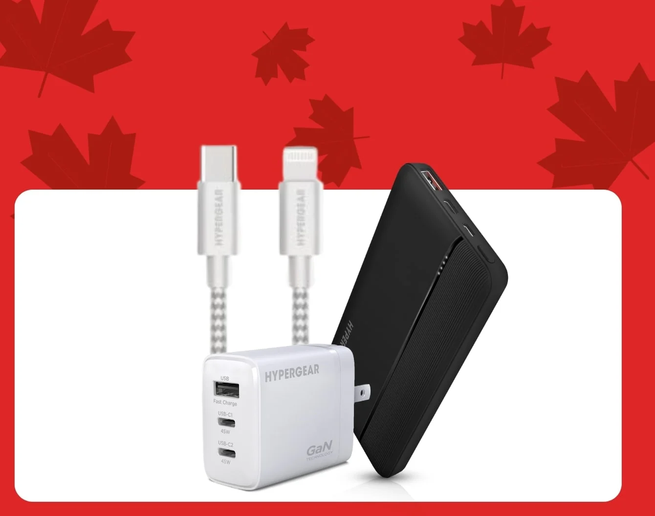 Des câbles Hypergear dans une boîte derrière une batterie externe Hypergear noire, à côté d'un bloc de recharge de téléphone Hypergear blanc, à l'intérieur d'un contenant blanc, sur un fond rouge couvert de feuilles d'érable rouge foncé.